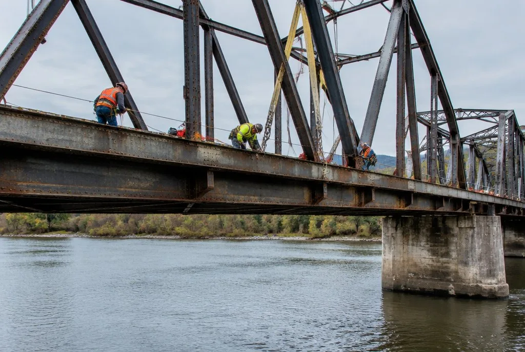 old steel bridge being repaired by workers over a river in the United States